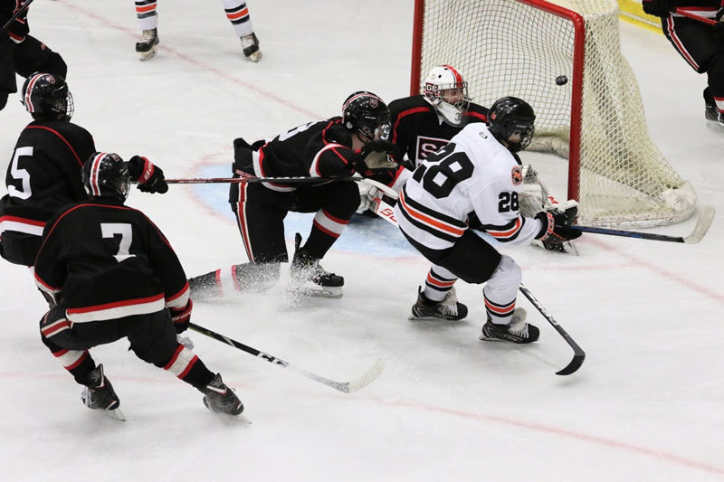 Multiple players work to regain control of a hockey puck as the goalie protects the goal. 