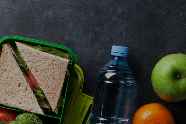 A picture of a sandwich on wheat bread with a bottle of water, an orange, and a Granny Smith apple.