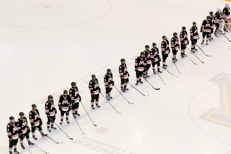 A picture of the hockey team in a line with their hockey sticks.