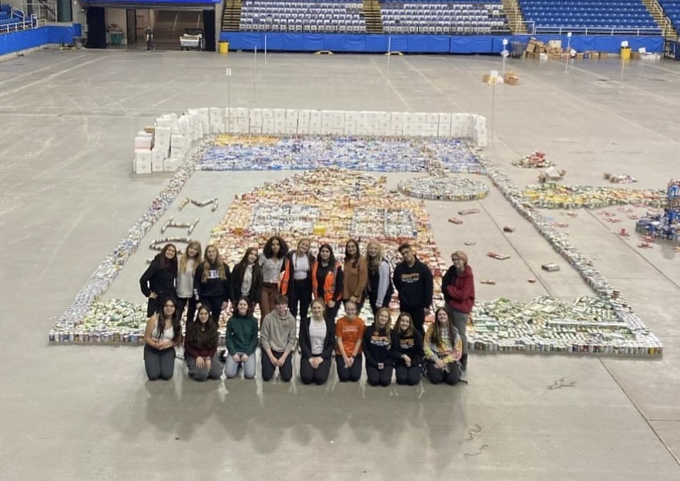 group of students poses in front of thousands of donated canned food items