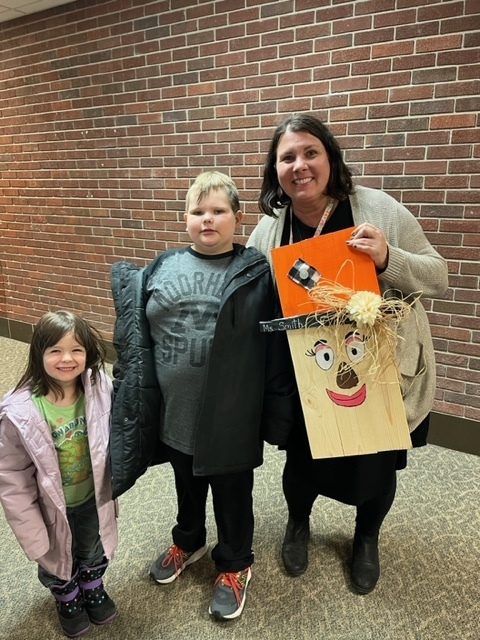 Students and teacher smiling and holding a scarecrow