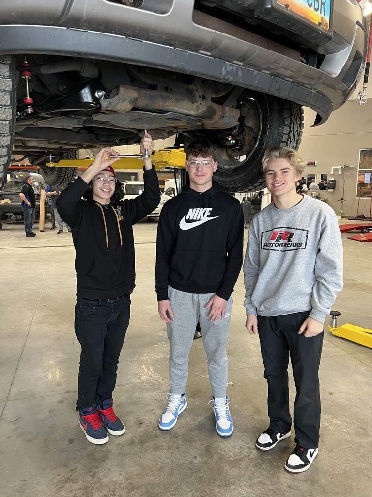 Students pose for a picture while fixing a car