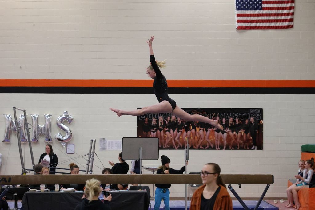 gymnast performs a split leap on the beam