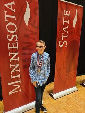 seventh grade student won first place stands in front of banners wearing medals. 